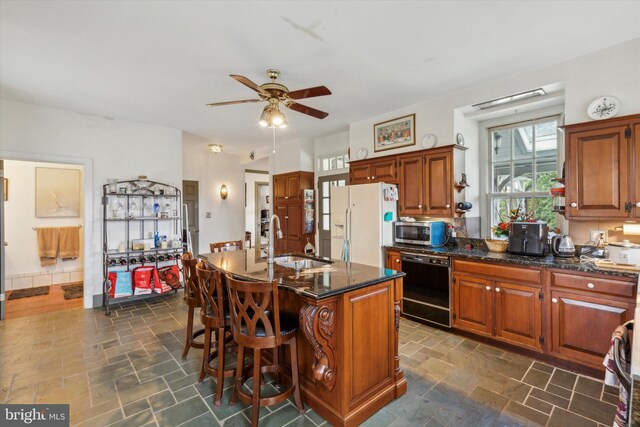 kitchen with white refrigerator with ice dispenser, a center island with sink, black dishwasher, sink, and ceiling fan