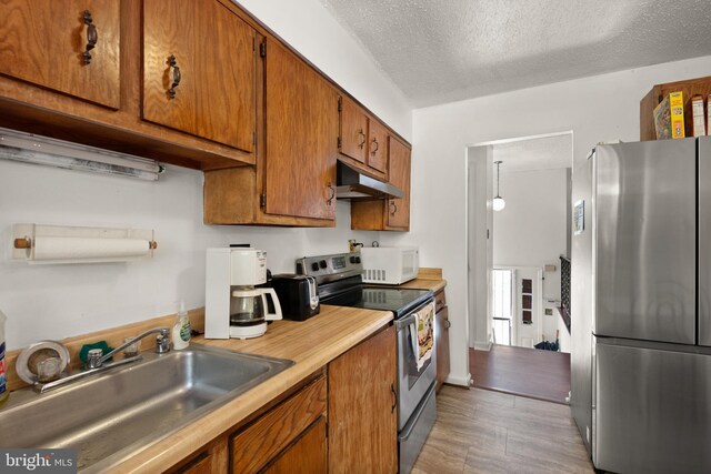 8600 Sapienza Dr, Fort Washington, MD 20744 - kitchen with appliances with stainless steel finishes, under cabinet range hood, a sink, brown cabinetry, and a textured ceiling