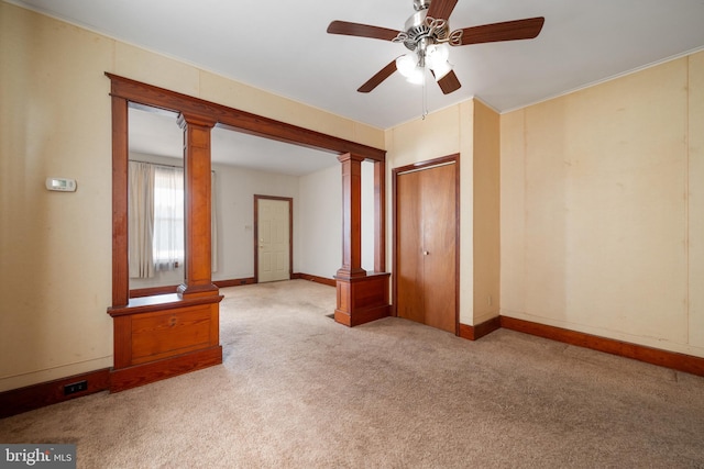 carpeted spare room with ornate columns, ornamental molding, and ceiling fan