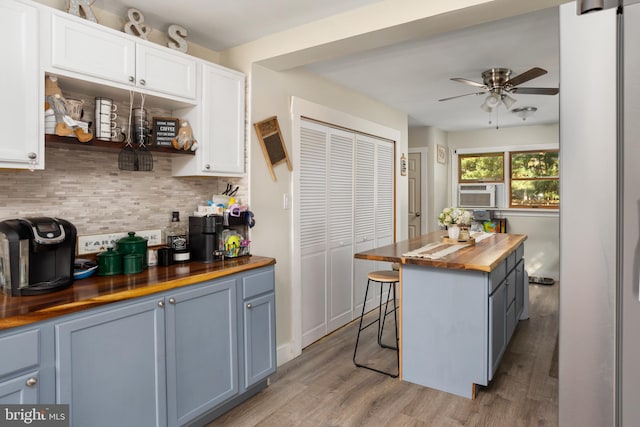 kitchen with cooling unit, butcher block counters, white cabinetry, a kitchen breakfast bar, and light hardwood / wood-style flooring