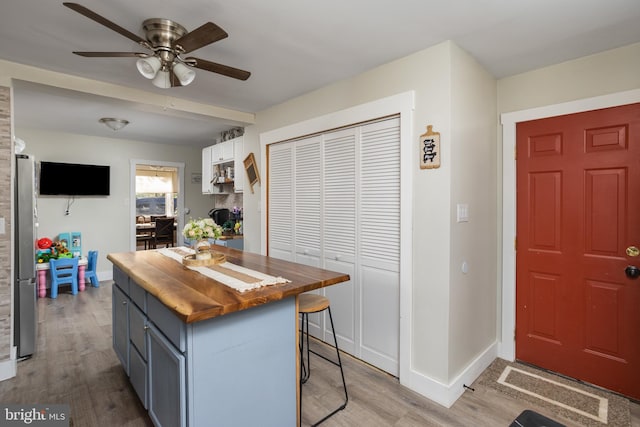 kitchen with light wood-type flooring, stainless steel refrigerator, wood counters, a breakfast bar, and white cabinets