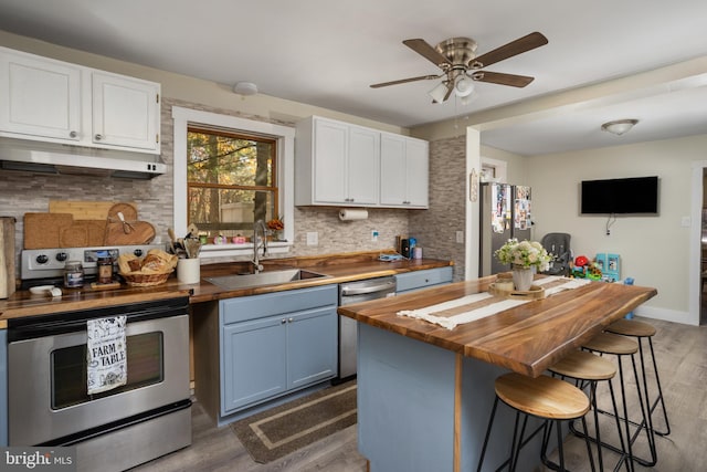 kitchen featuring butcher block counters, sink, appliances with stainless steel finishes, blue cabinetry, and white cabinets