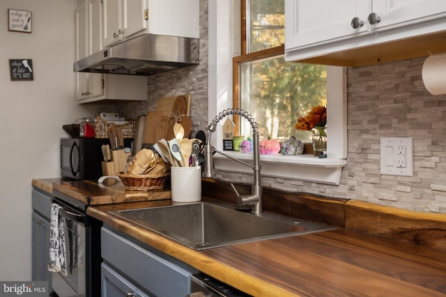 kitchen featuring butcher block countertops, decorative backsplash, white cabinetry, and sink