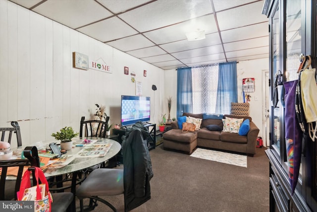 living room featuring wood walls, a drop ceiling, and dark carpet