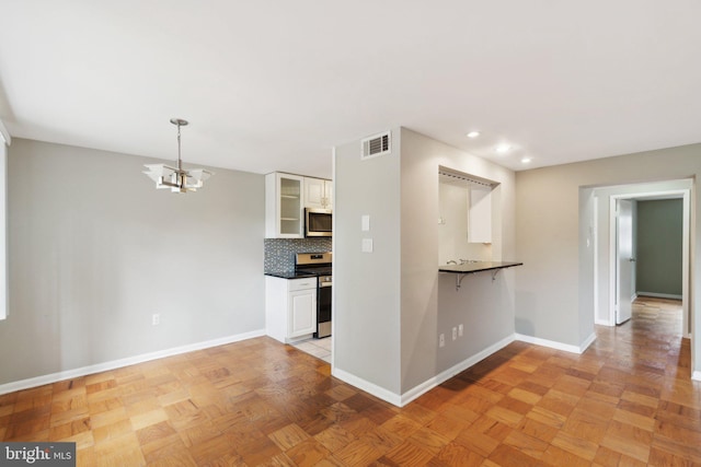 kitchen featuring stainless steel appliances, white cabinets, backsplash, and a notable chandelier