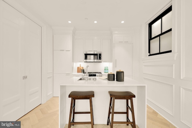 kitchen with a kitchen bar, white cabinetry, appliances with stainless steel finishes, and an island with sink