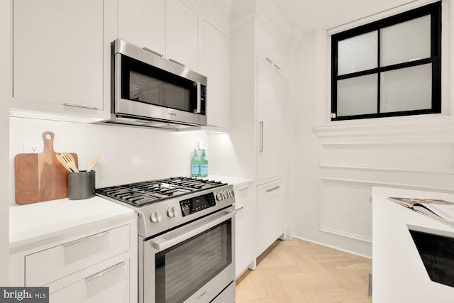 kitchen with light parquet floors, white cabinetry, and appliances with stainless steel finishes