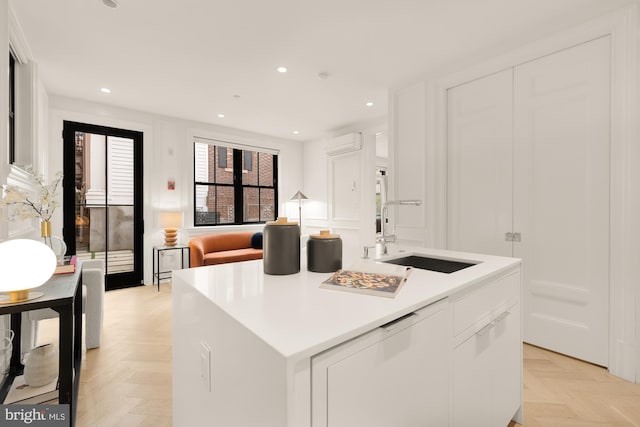 kitchen featuring an island with sink, white cabinets, sink, and light parquet floors