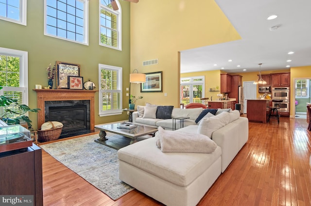 living room featuring a towering ceiling, a premium fireplace, and light hardwood / wood-style flooring