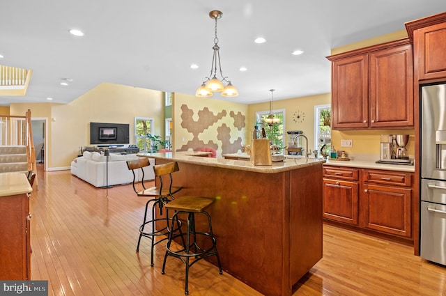 kitchen with light wood-type flooring, a notable chandelier, stainless steel refrigerator with ice dispenser, hanging light fixtures, and a kitchen breakfast bar