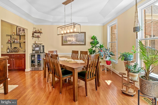 dining space with wine cooler, light wood-type flooring, crown molding, and a raised ceiling