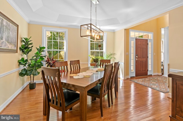 dining area with a notable chandelier, light wood-type flooring, crown molding, and a tray ceiling