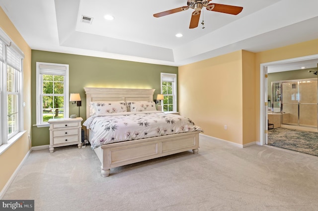 bedroom featuring multiple windows, light colored carpet, ceiling fan, and ensuite bath