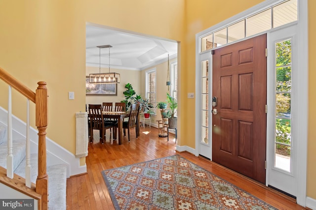 entrance foyer with wood-type flooring, a raised ceiling, and crown molding