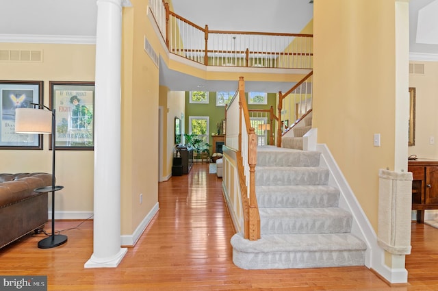 stairs with ornamental molding, hardwood / wood-style floors, a towering ceiling, and decorative columns