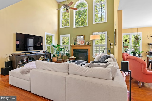 living room with ceiling fan, a towering ceiling, a healthy amount of sunlight, and light hardwood / wood-style flooring