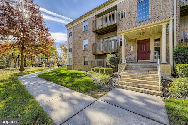 view of exterior entry featuring a lawn and a balcony