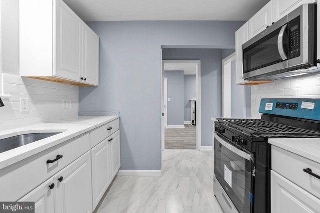 kitchen with range with gas stovetop, decorative backsplash, white cabinetry, and sink