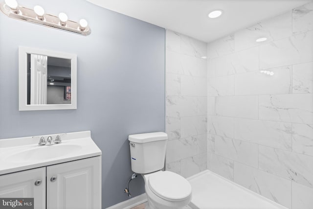 bathroom featuring a tile shower, vanity, and toilet