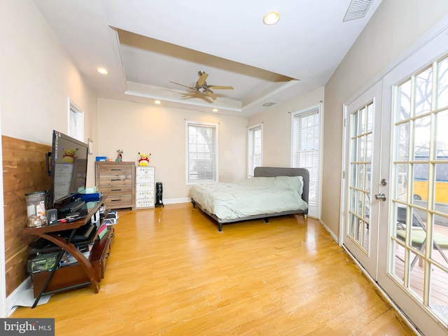 bedroom featuring ceiling fan, access to exterior, a raised ceiling, light wood-type flooring, and french doors