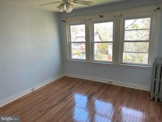 unfurnished room with dark wood-type flooring, radiator, a wealth of natural light, and ceiling fan