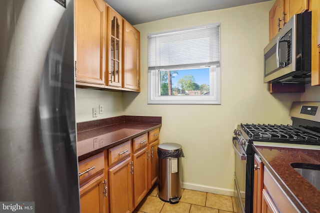 kitchen with stainless steel appliances, dark stone counters, and light tile patterned flooring