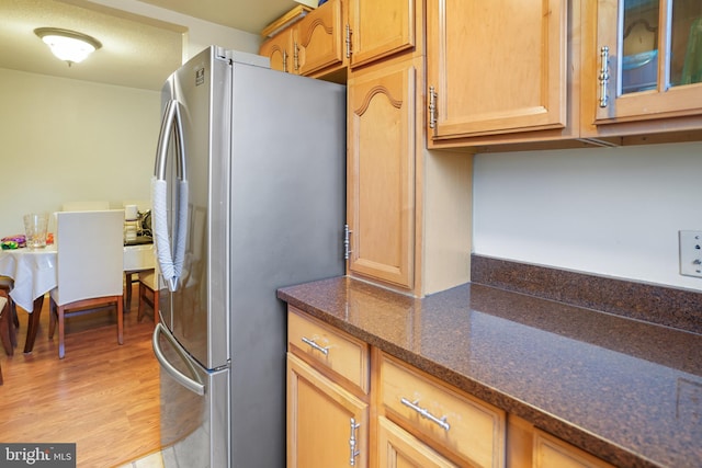 kitchen featuring light wood-type flooring, stainless steel refrigerator, and dark stone counters