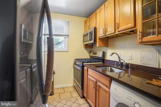 kitchen with sink, dark stone countertops, light tile patterned flooring, washer / dryer, and stainless steel appliances