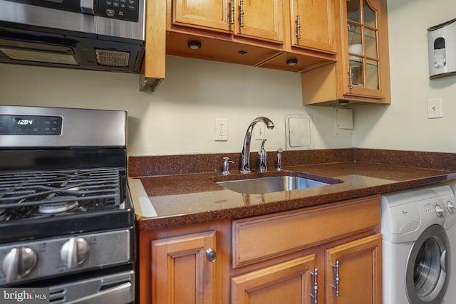 kitchen with washer / dryer, stainless steel appliances, dark stone countertops, and sink