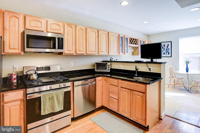 kitchen featuring light hardwood / wood-style floors, kitchen peninsula, sink, appliances with stainless steel finishes, and light brown cabinetry