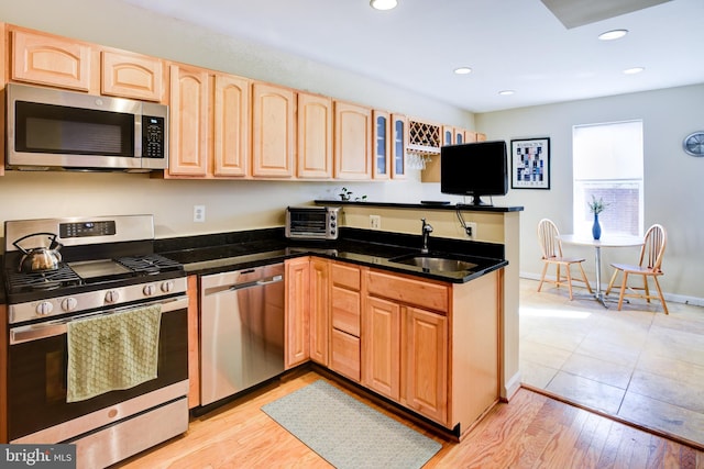 kitchen featuring kitchen peninsula, appliances with stainless steel finishes, sink, and light hardwood / wood-style flooring