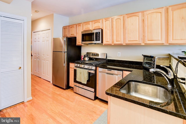 kitchen featuring light hardwood / wood-style floors, sink, appliances with stainless steel finishes, light brown cabinetry, and dark stone countertops