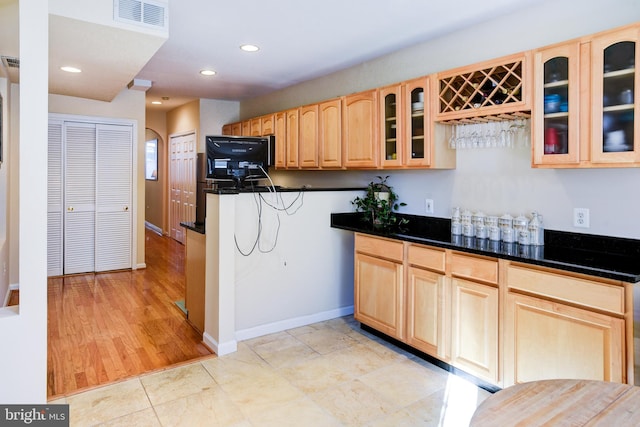 kitchen featuring light brown cabinetry, dark stone countertops, and light wood-type flooring