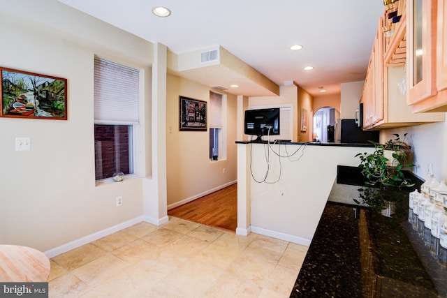 kitchen with kitchen peninsula, fridge, and dark stone countertops