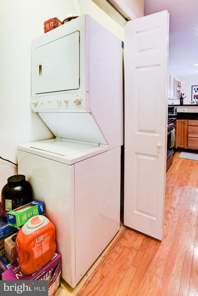 laundry area with light wood-type flooring and stacked washer / drying machine