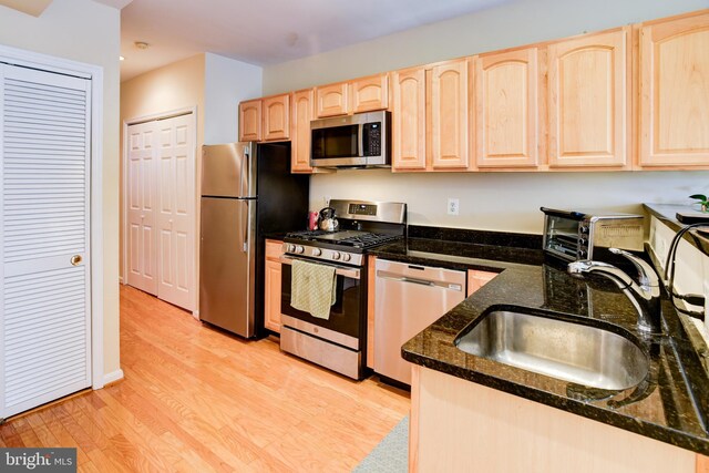 kitchen with stainless steel appliances, light brown cabinets, sink, dark stone countertops, and light hardwood / wood-style flooring