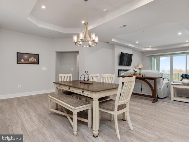 dining room with an inviting chandelier, a raised ceiling, and light hardwood / wood-style flooring