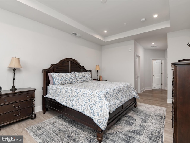 bedroom with a tray ceiling and light hardwood / wood-style floors