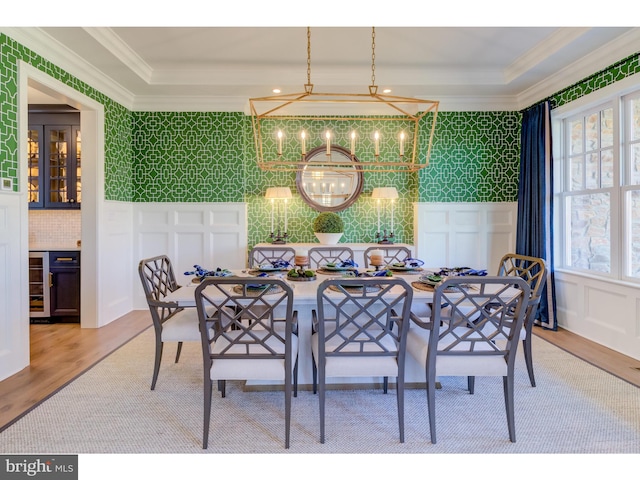 dining room featuring beverage cooler, light wood-type flooring, an inviting chandelier, and crown molding