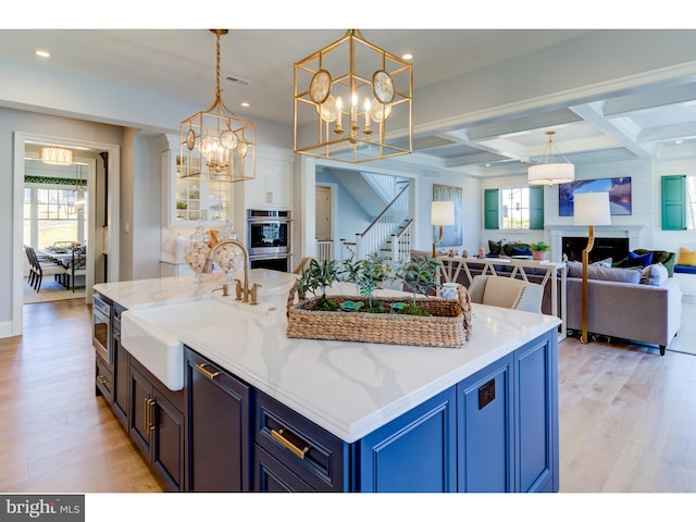 kitchen with sink, coffered ceiling, double oven, pendant lighting, and light wood-type flooring