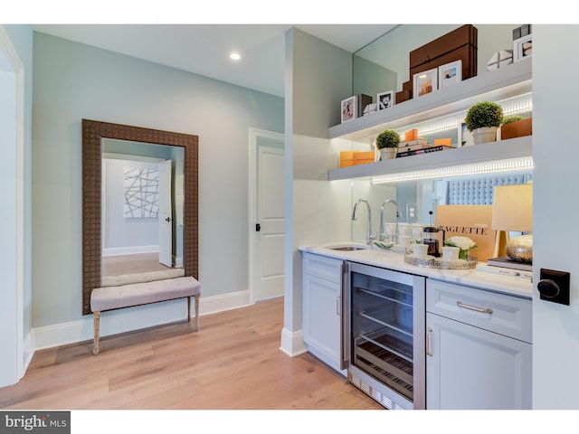 bar with wine cooler, white cabinetry, light wood-type flooring, and sink