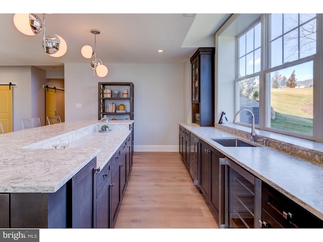 kitchen with light hardwood / wood-style floors, beverage cooler, a barn door, sink, and decorative light fixtures