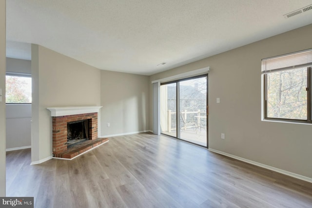 unfurnished living room featuring a brick fireplace, plenty of natural light, and light wood-type flooring