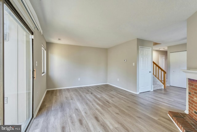 unfurnished living room with a brick fireplace, light hardwood / wood-style flooring, and a textured ceiling