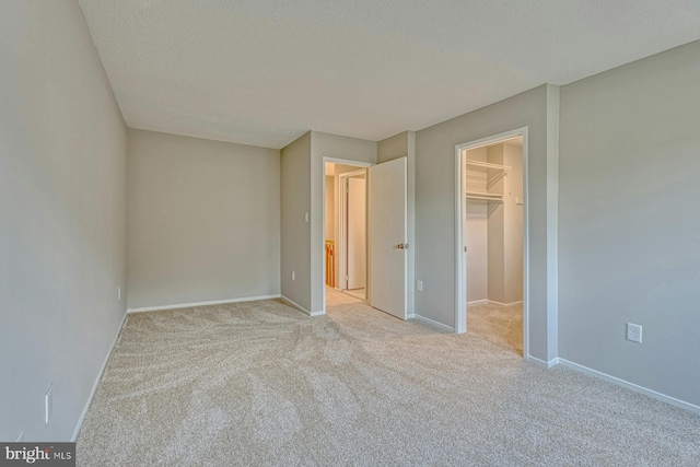 unfurnished bedroom with light colored carpet, a textured ceiling, a closet, and a walk in closet