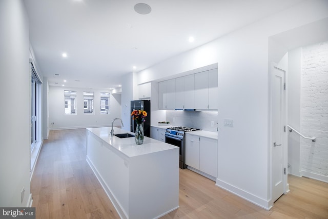 kitchen with an island with sink, light hardwood / wood-style floors, black refrigerator, and gas range