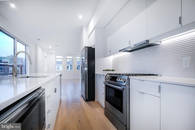 kitchen with white cabinetry, extractor fan, appliances with stainless steel finishes, light wood-type flooring, and sink