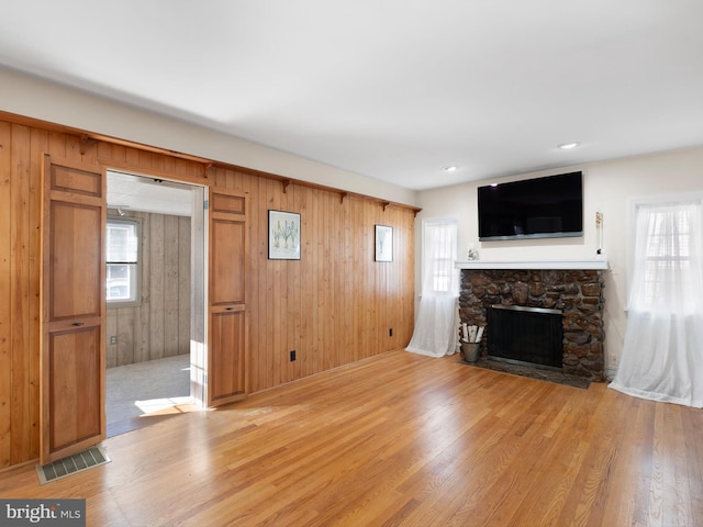 unfurnished living room with a stone fireplace, wooden walls, and light hardwood / wood-style flooring