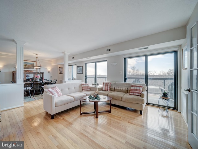 living room featuring light hardwood / wood-style flooring, ornate columns, and a textured ceiling