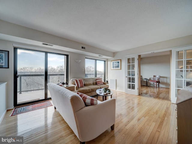 living room with light hardwood / wood-style floors, french doors, and a textured ceiling